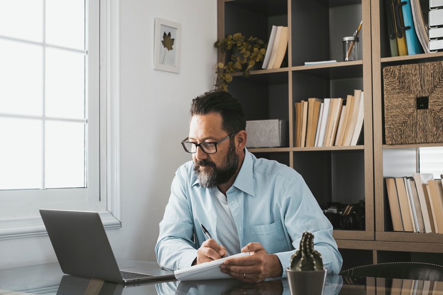 Uomo adulto che guarda il pc e scrive su un foglio di carta