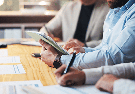 Persone sedute ad un tavolo, uno che scrive e uno che sfoglia pagine