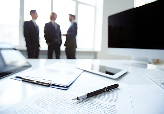 Primo piano di fogli su una scrivania, tre persone sullo sfondo che discutono